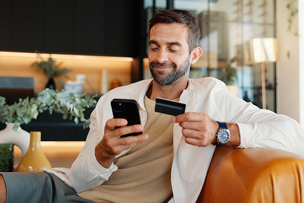A man sitting on a couch, focused on his smartphone, exploring strategies to build credit fast
