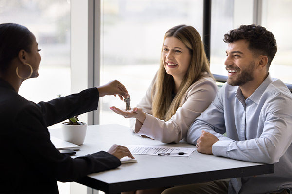 A man hands a key to a woman at a table, symbolizing their participation in first-time home buyer programs in South Texas.