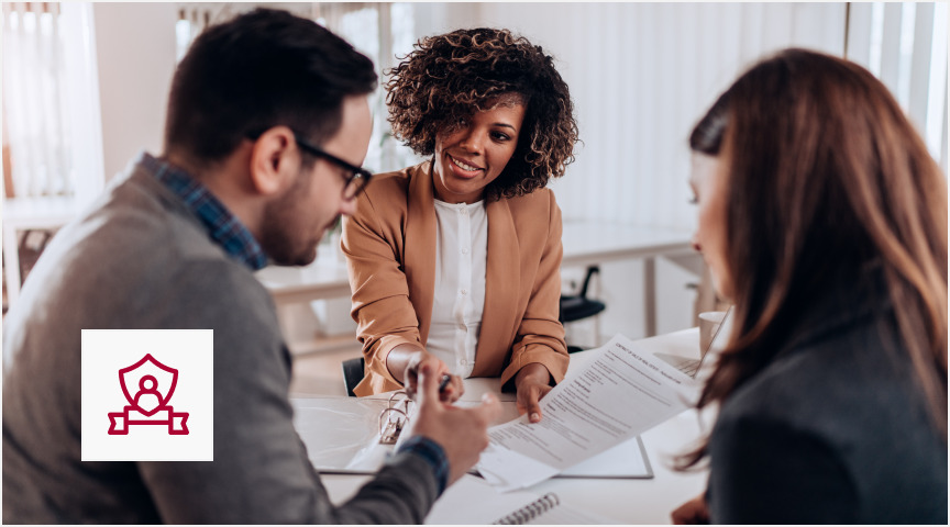 A real estate agent and a client engaged in conversation at a desk in a professional office environment.