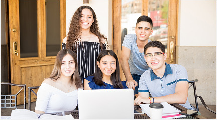 A group of four young individuals seated at a table, collaborating while using a laptop.