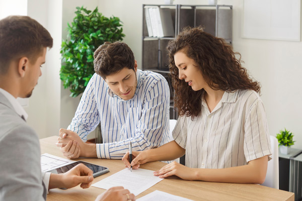 Cheerful Caucasian couple signing a contract reaching agreement with a man realtor or financial advisor sitting at desk on workplace. Insurance agent making a deal in office with clients.