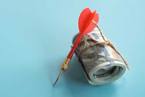 Red dart leaning against a roll of US dollar bills for financial targeting.