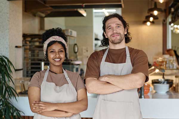 Smiling caucasian man and joyful black woman standing together at their workplace at cafeteria